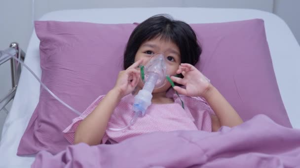 A little Asian girl has an oxygen mask and breathing through a nebulizer at the hospital. Concept of bronchitis, respiratory and Medical treatment, inhaling medicine, mist, from a nebulizer. - Footage, Video