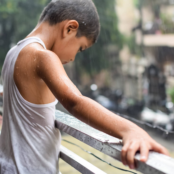 家のバルコニーで夏の雨の中で遊んでいる小さな子供、モンスーン雨の季節の間に雨の滴で遊んでいるインドの賢い男の子、雨の中で遊んでいる子供 - 写真・画像