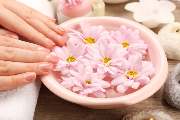 Vrouwelijke handen en kom met spa water met bloemen, close-up - Foto, afbeelding