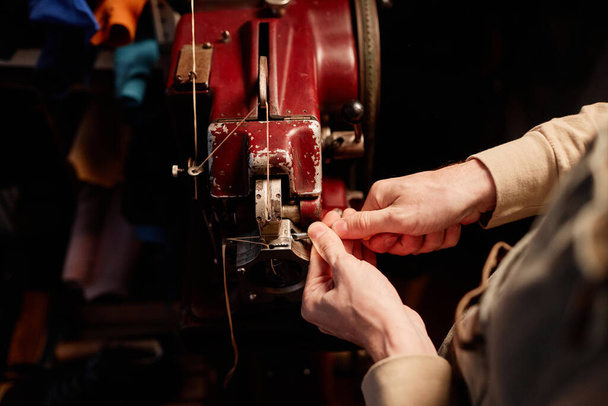 Vue ci-dessus du jeune artisan mâle dans le tablier de fixation des détails de la machine à coudre électrique tout en se tenant devant l'équipement dans l'atelier - Photo, image