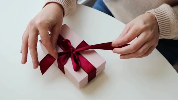 女性の手は贈り物を包む ソフトピンク色の赤いリボンを閉じる - 映像、動画