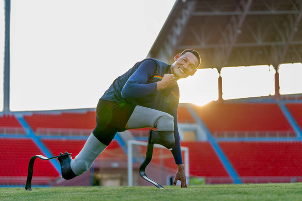 Gros plan vue de côté sport homme athlète prothèse jambes rester dans la position d'étirement aussi regarder la caméra dans le stade avec la lumière douce de la soirée. - Photo, image