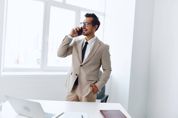 Öltöny férfi boldog hívás telefon ülő életmód foglalkozás dolgozó íróasztal mobil iroda laptop mosoly telefon beszélgetés üzletember videó nyertes vonzó számítógép - Fotó, kép