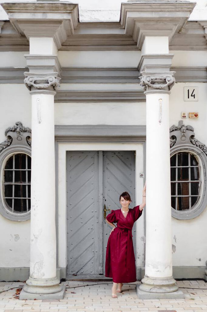 Muchacha atractiva con peinado, en vestido rojo está caminando en la calle en el fondo del edificio viejo. - Foto, Imagen