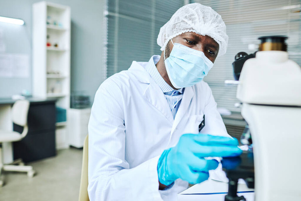 Πορτρέτο του εστιασμένου μαύρου άνδρα φορώντας μάσκα προσώπου, ενώ κάνει έρευνα στο ιατρικό εργαστήριο - Φωτογραφία, εικόνα