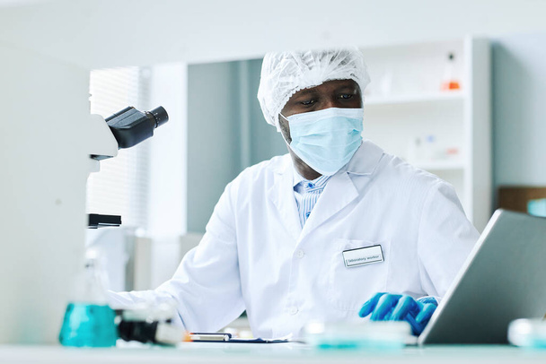 Muotokuva musta mies tekee tieteellistä tutkimusta laboratoriossa ja yllään kasvonaamio - Valokuva, kuva