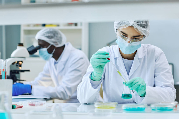 Porträt einer jungen Wissenschaftlerin, die mit farbigen Proben arbeitet, während sie medizinische Forschung im Labor betreibt, Kopierraum - Foto, Bild