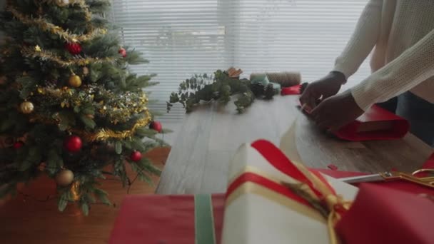 Panera de persona irreconocible preparando regalo para Navidad usando papel de regalo rojo en la mesa - Imágenes, Vídeo