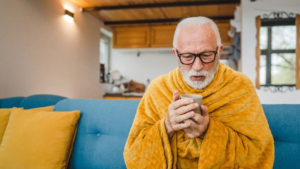 un homme âgé caucasien assis sur le canapé-lit à la maison tenir tasse de thé froid commun éternuer malade attrapé froid - Photo, image