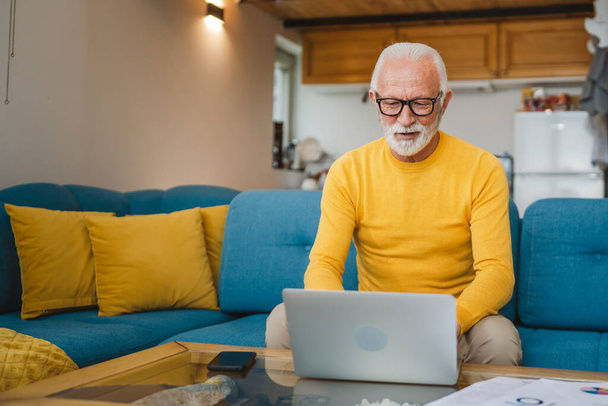 髭と眼鏡を持つ一人のシニア白人男性祖父は自宅でノートパソコンの使用コンピュータで動作します - 写真・画像