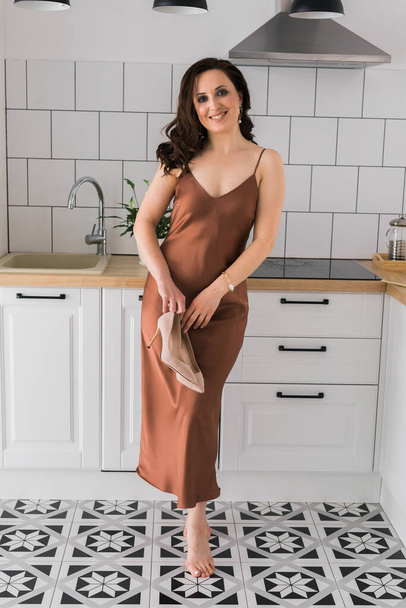 Jolie jeune femme souriante portant une robe longue en soie dansant à la cuisine à la maison - Photo, image