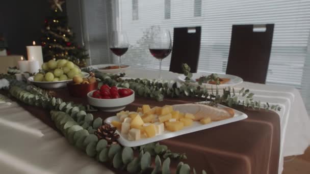 Middelmatige close-up van kaasblokjes, ham plakjes, tomaten, wijn en hapjes op feestelijke tafel bereid voor kerstfeest in gezellige woonkamer - Video
