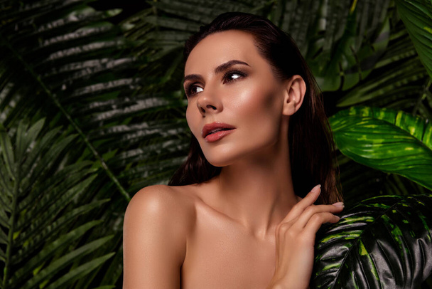 Портрет приголомшливої чуттєвої красивої жінки, яка торкається її шкіри в оазисному курорті, ховається на пальмовому листі джунглів. - Фото, зображення