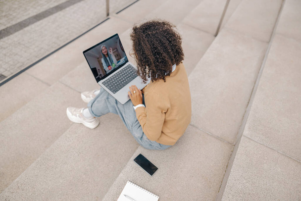 Female freelancer have a video conference with colleague sitting on stairs outside - Photo, Image