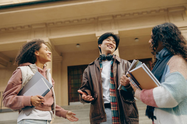 Jonge studenten praten en lachen samen buiten staan bij de campus en boeken bijhouden  - Foto, afbeelding