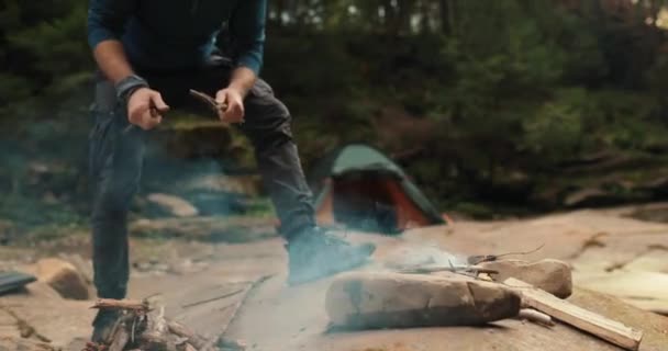 Samiec turysty rąbie drewno na opał małym toporem przy ognisku w lesie. Podróżnik przygotowuje drewno na ogień. Człowiek w dziczy. turysta na świeżym powietrzu, przetrwanie na pustkowiu, ognisko - Materiał filmowy, wideo