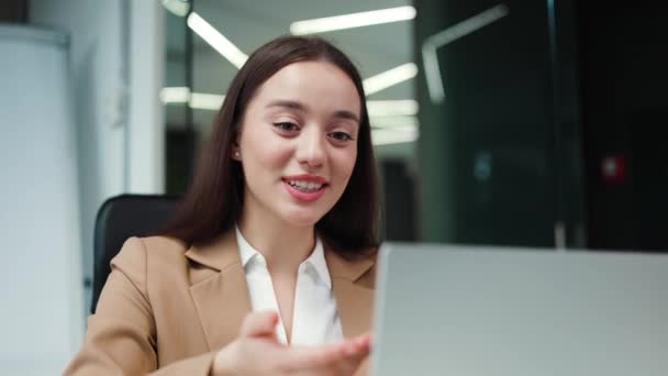Successful brunette manager in business suit using portable laptop to conducting online meeting and talking with colleagues. Competent beautiful caucasian female working inside modern office. - Footage, Video