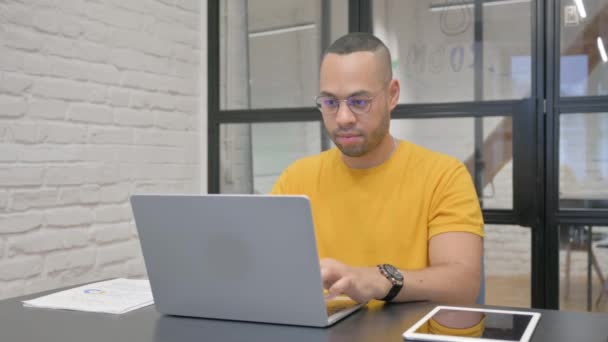 Spanyol férfi mosolyog a kamera, miközben dolgozik a laptop az irodában - Felvétel, videó