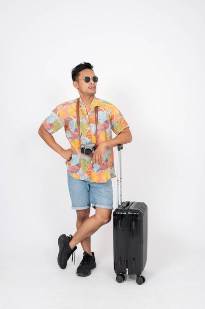 Mutsuz bir Asyalı turist, havaalanında uzun süre bekledikten sonra bavullarıyla birlikte izole edilmiş beyaz bir arka planda beklemekten memnun değil.. - Fotoğraf, Görsel