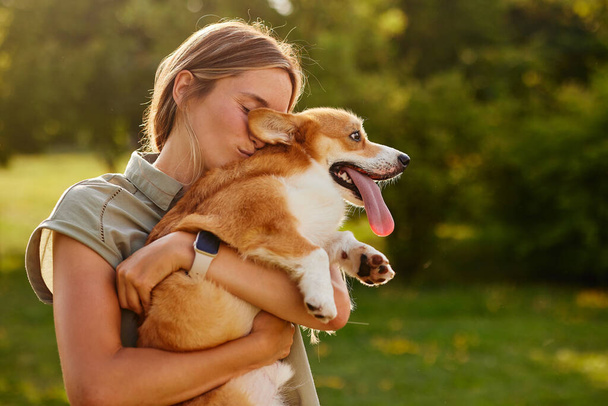 young girl hugging pembroke welsh corgi in the park in sunny weather, happy dogs concept - Photo, Image