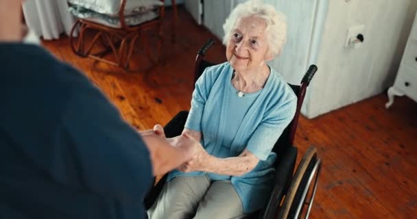 Persona anziana, infermiera e si tiene per mano in sedia a rotelle per il sostegno, la cura e l'empatia in pensione. Persone, badante e anziani con disabilità, riabilitazione e gentilezza nella casa di cura. - Filmati, video
