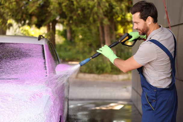 Worker washing auto with high pressure water jet at outdoor car wash - Photo, Image