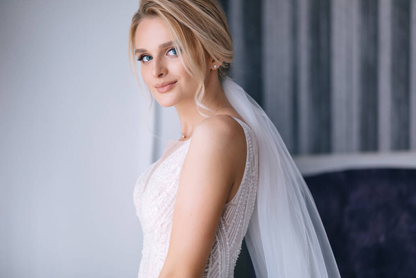 young girl in a white dress at home with a veil. Bride with luxurious hair and makeup. Preparing the bride for the upcoming wedding. - Photo, Image