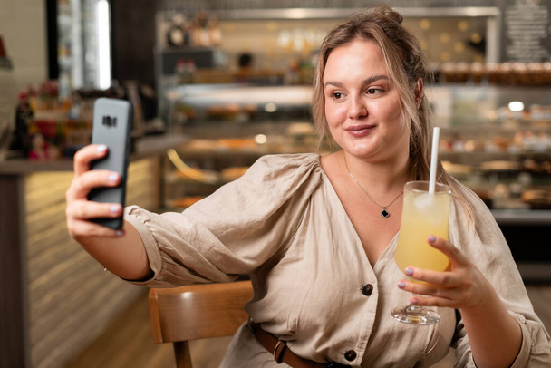 Концепция социального влияния. портрет женщины, держащей коктейль в руке и сидящей в кафе с селфи. Копирование пространства - Фото, изображение