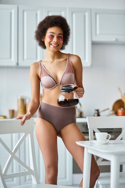 rizado feliz afroamericana mujer con parches para los ojos de pie en ropa interior con cafetera - Foto, Imagen