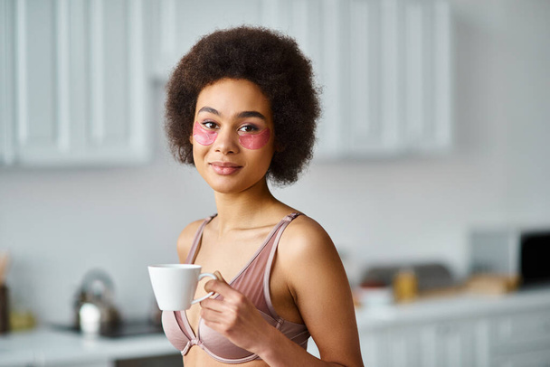 довольно африканская американка с повязками на глазу, стоящая в нижнем белье и наслаждающаяся кофе в чашке - Фото, изображение