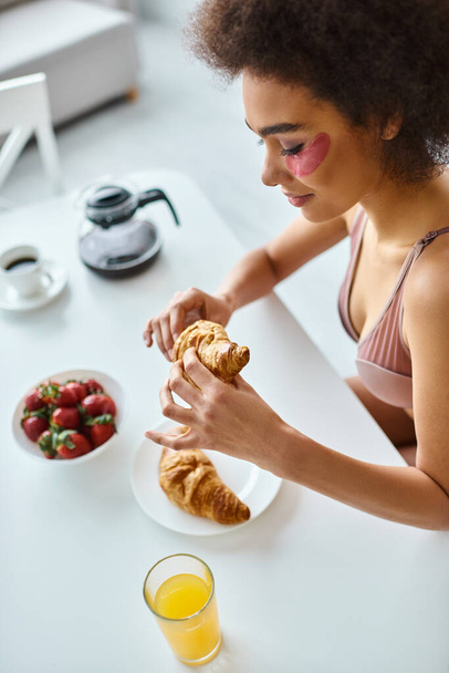 happy african american woman holding freshly baked croissant during breakfast in kitchen, top view - Photo, Image