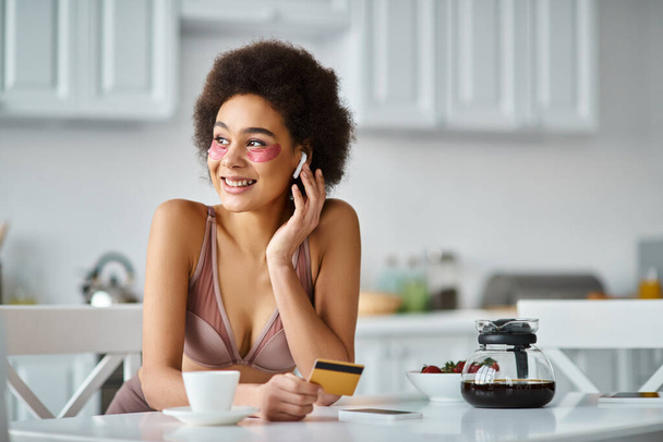 mujer afroamericana feliz en auriculares con parches bajo los ojos de compras en línea con tarjeta de crédito - Foto, imagen
