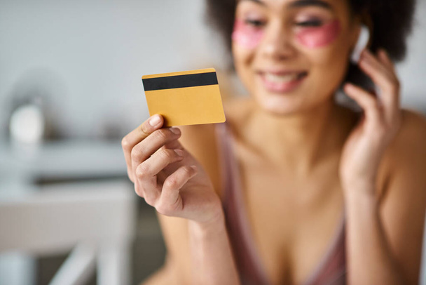 wazig Afrikaans amerikaanse vrouw in koptelefoon winkelen van thuis met haar creditcard - Foto, afbeelding