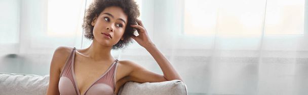 Gedachte jonge Afrikaanse Amerikaanse vrouw loungen in lingerie op een bank thuis, horizontale banner - Foto, afbeelding