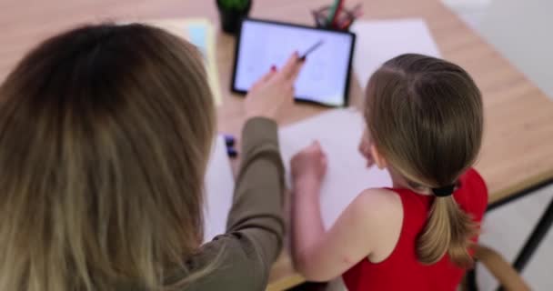Kind, meisje en volwassene zitten aan tafel en maken huiswerk met behulp van tablet. Meisje doet huiswerk of online onderwijs - Video