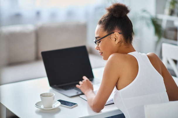 σγουρή αφροαμερικανή γυναίκα με γυαλιά που εργάζονται από το σπίτι στο laptop της, επιχειρηματίας - Φωτογραφία, εικόνα