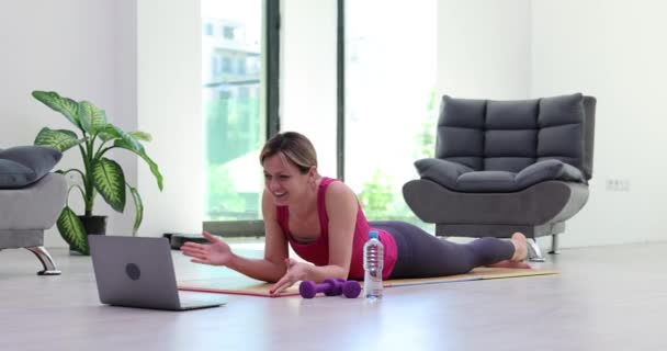 Mujer en ropa de fitness está teniendo una videoconferencia en línea en el ordenador portátil. Entrenamiento de fitness en casa en estera y deporte blogs de fitness - Imágenes, Vídeo