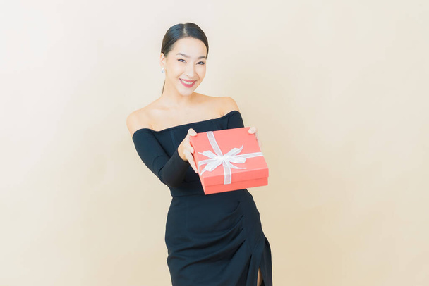 Портрет красива молода азіатка посміхається з червоною подарунковою коробкою на кольоровому фоні
 - Фото, зображення