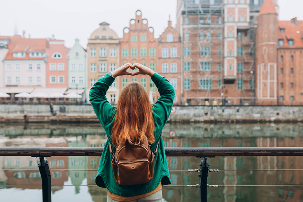 Avontuurlijke vrouwen maken door handen in de vorm van liefde hart. Aantrekkelijke jonge vrouwelijke toerist verkent nieuwe stad. Reizen door Europa in het najaar. - Foto, afbeelding