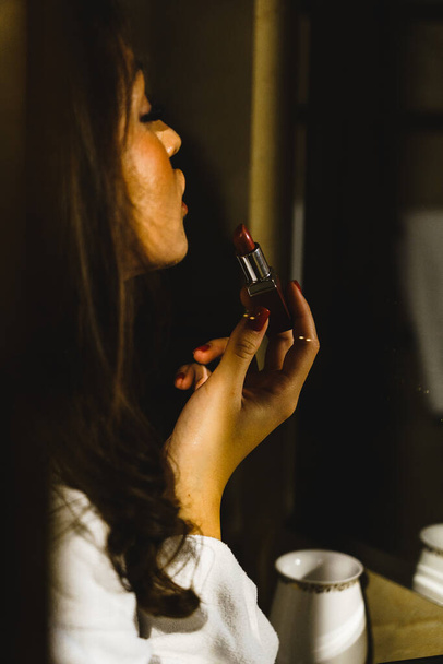 Молодая женщина в халате красит губы в ванной комнате.Концепция отдыха в отеле - Фото, изображение
