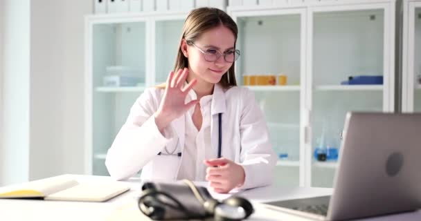 Online βιντεοκλήση του γιατρού με τους ασθενείς. Γιατρός θεραπευτής κουνώντας το χέρι μπροστά από το φορητό υπολογιστή, χαιρετώντας ασθενή - Πλάνα, βίντεο