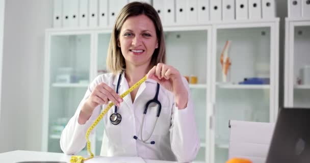 Médico dietista sonriente sosteniendo una cinta métrica en la clínica. Nutrición y dieta adecuadas - Imágenes, Vídeo