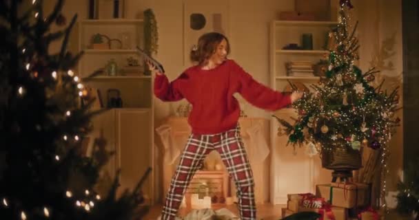 Mujer joven feliz con tableta digital bailando en casa mientras disfruta de la víspera de Navidad - Metraje, vídeo