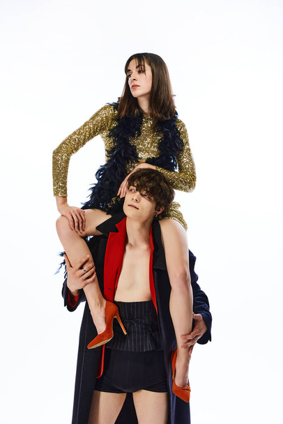 Portrait of young girl in holiday dress sits on guys shoulders and turns his head as she wants against white studio background. Concept of bizarre love, fashion, glamour, New Year, Valentines Day. - Foto, immagini
