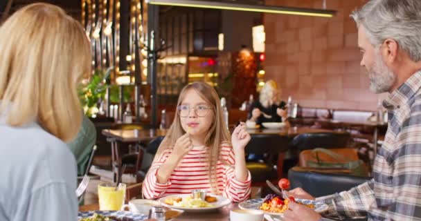 Zoomer sur la petite fille caucasienne avec des lunettes pour une meilleure vision manger des frites savoureuses avec du ketchup tout en étant assis avec ses parents dans un café ou une pizzeria. Bonne famille passer un bon week-end au café. - Séquence, vidéo