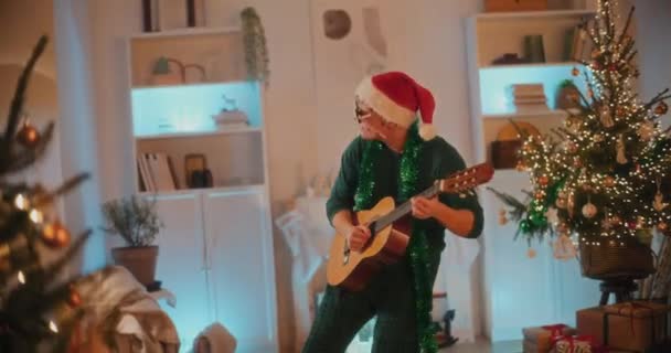 Young man enjoys playing guitar while standing in living room during Christmas - Footage, Video