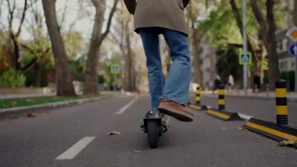 Вид ззаду на стильну жінку їде електричний скутер на міській дорозі. Обрізаний вид на молоду жінку в джинсах і куртці з використанням екологічного транспорту. Активне дозвілля. Міський спосіб життя - Кадри, відео