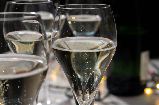 Novoroční party, malé bublinky brut šampaňského cava nebo Státní prokuratura vína v tulipánových brýlích s věnec světla na tmavém pozadí - Fotografie, Obrázek