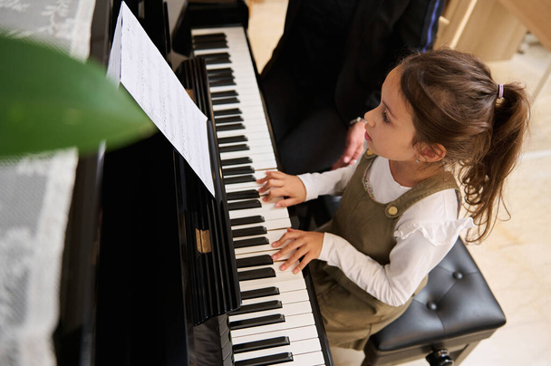 Top view egy kis zongorista lány zongorázik, komponál egy dallamot irányítása alatt tanára során egyéni zenei leckét otthon. Gyerekek. Oktatás. Életstílus. Hobbi és szórakozás - Fotó, kép