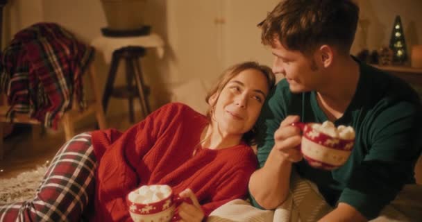 Hymyilevä nainen tilalla kuppi vaahtokarkkeja poikaystävä olohuoneessa joulun aikana - Materiaali, video